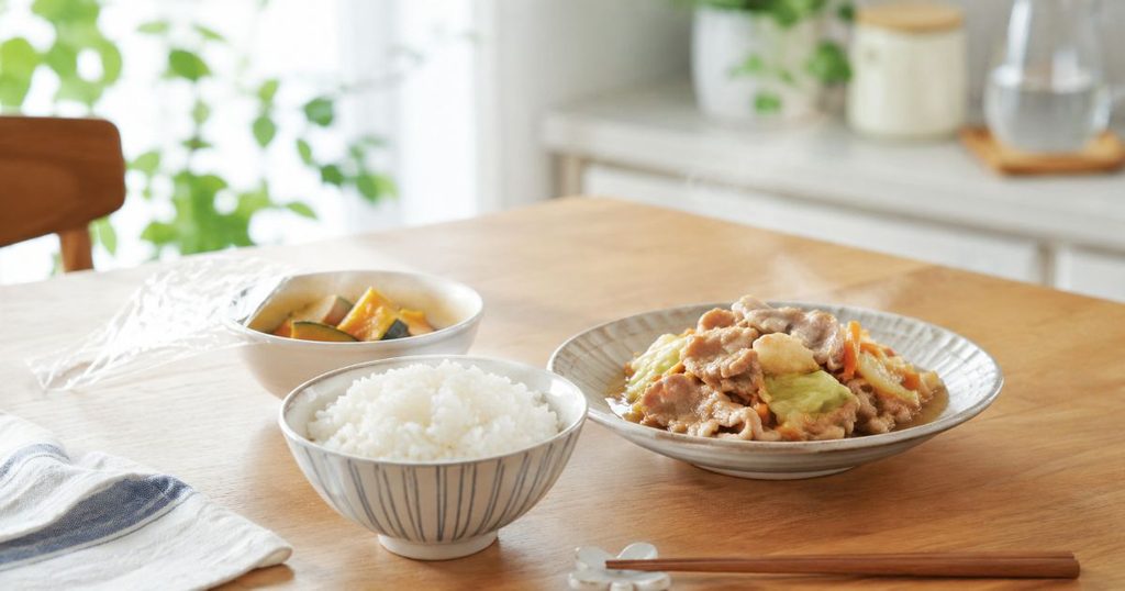 湯気の立つごはんとおかずを並べた食卓